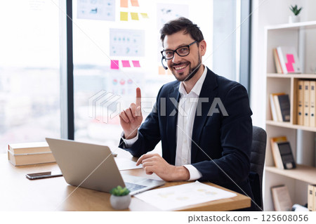 Businessman in his thirties wearing headset working in office on video call using laptop 125608056