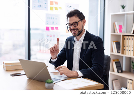 Businessman in his thirties wearing headset working in office on video call using laptop Businessman in his thirties wearing headset working in office on video call using laptop 125608060