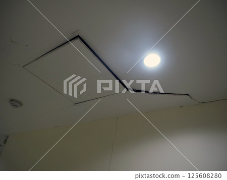 A damaged ceiling in hallway with cracks and visible gap, showcasing structural issues and poor maintenance 125608280