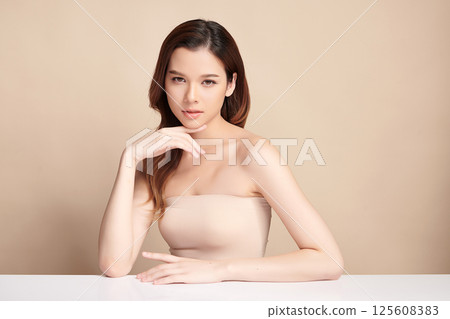 A beautiful young Asian woman with clean, fresh skin against a beige background. Skincare, facial treatment, cosmetology, beauty, and spa. An elegant portrait of an Asian woman. 125608383