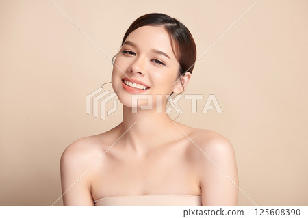 A beautiful young Asian woman with clean, fresh skin against a beige background. Skincare, facial treatment, cosmetology, beauty, and spa. An elegant portrait of an Asian woman. 125608390