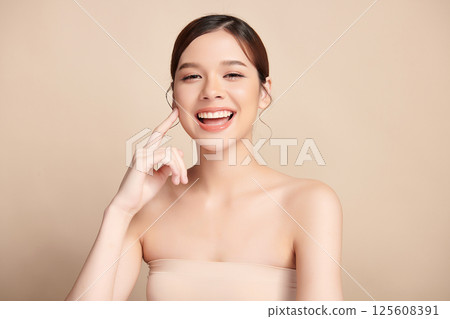 A beautiful young Asian woman with clean, fresh skin against a beige background. Skincare, facial treatment, cosmetology, beauty, and spa. An elegant portrait of an Asian woman. 125608391