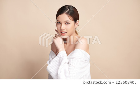 A beautiful young Asian woman with clean, fresh skin against a beige background. Skincare, facial treatment, cosmetology, beauty, and spa. An elegant portrait of an Asian woman. 125608403