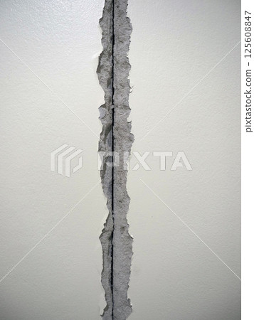 A damaged wall with visible crack, showing torn paper and exposed surface underneath, creating distressed appearance 125608847