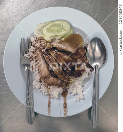 A delicious plate of rice topped with tender meat, savory sauce, and fresh cucumber slices, evoking sense of comfort and satisfaction A delicious plate of rice topped with tender meat, savory sauce, and fresh cucumber slices, evoking sense of comfort and satisfaction 125608848