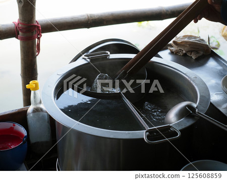 A cooking noodles in steaming pot, hand holds ladle while another uses strainer to lift noodles. scene captures essence of street food preparation 125608859