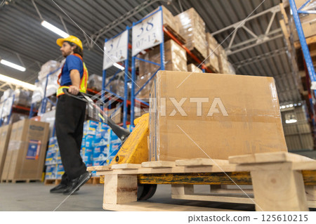Close up cardboard crate, Man worker wear safety uniform push load cart goods to shelf in store. Company employees arrange products. Warehouse industrial stock storage. 125610215