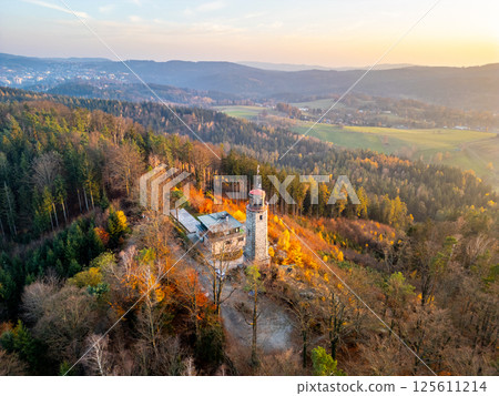 The lookout tower on Prosec Ridge near Jablonec nad Nisou captures the essence of autumn as the sun sets, casting golden hues over the vibrant landscape of the Jizera Mountains. 125611214