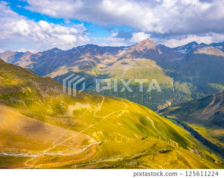Breathtaking view of the Otztal Alps showcasing rolling green hills and majestic peaks under a partly cloudy sky. Perfect day for hiking and exploring nature's beauty in Austria. 125611224