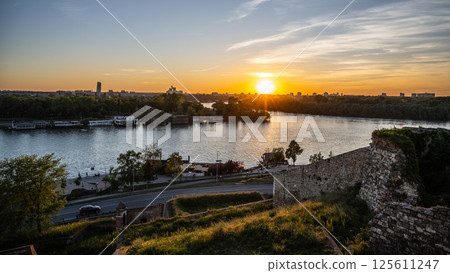 A breathtaking view of the Sava River at sunset from the historic Kalamegdan Fortress in Belgrade, Serbia. The sun sets behind distant hills, casting warm hues over the water. A breathtaking view of the Sava River at sunset from the historic Kalamegdan Fortress in Belgrade, Serbia. The sun sets behind distant hills, casting warm hues over the water. 125611247