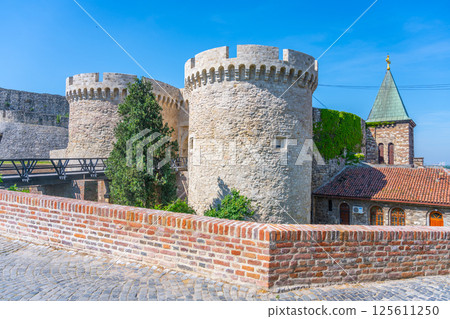 Zindan Gate stands as a historical landmark within Belgrade Fortress, showcasing its impressive architecture against a bright blue sky. Visitors can admire the stone towers and surrounding greenery. 125611250
