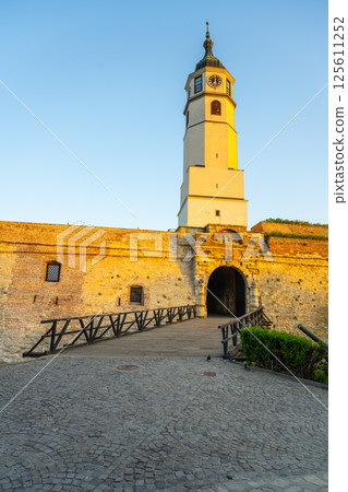 The Clock Tower and Clock Gate stand majestically at Kalemegdan Fortress, illuminated by the warm hues of sunset, showcasing the rich history and architecture of Belgrade, Serbia. 125611252