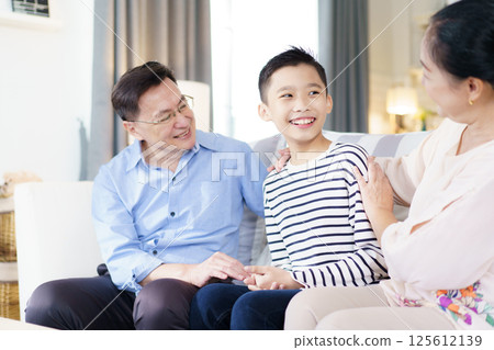 Asian family with father, mother, and son staying in living room together. Happy Asian family staying together in the living room. Parent is talking with their son while relaxing in living room.  125612139