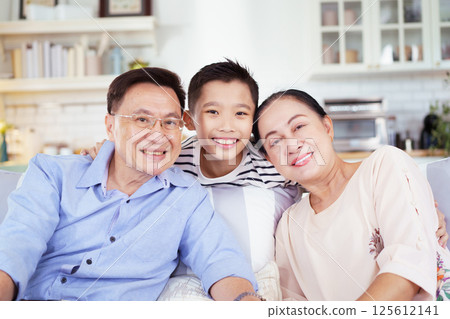 Asian family with father, mother, and son staying in living room together. Happy Asian family staying together in the living room. Parent is talking with their son while relaxing in living room.  125612141