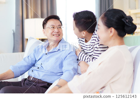 Asian family with father, mother, and son staying in living room together. Happy Asian family staying together in the living room. Parent is talking with their son while relaxing in living room. Asian family with father, mother, and son staying in living room together. Happy Asian family staying together in the living room. Parent is talking with their son while relaxing in living room. 125612143