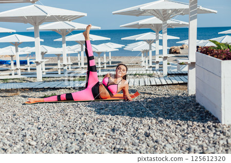 woman in tracksuit doing gymnastics yoga asana on the beach by the sea 125612320