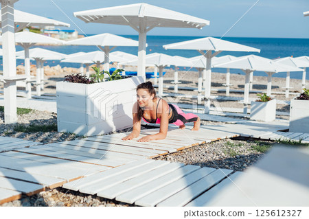 woman in tracksuit doing gymnastics yoga asana on the beach by the sea woman in tracksuit doing gymnastics yoga asana on the beach by the sea 125612327