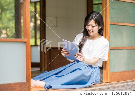 Young woman laughing while looking at a tablet in an old house 125612984