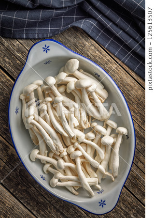 Raw white shimeji mushrooms in bowl on wooden table. Top view. 125613507