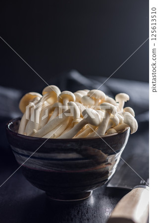 Raw white shimeji mushrooms in bowl on black table. 125613510