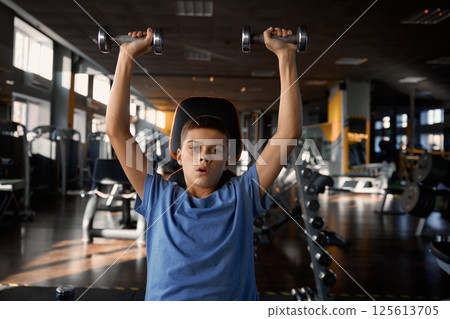Teen boy lifting dumbbells enjoying sportive workout at gym Teen boy lifting dumbbells enjoying sportive workout at gym 125613705