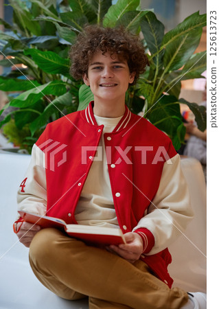 Handsome teenage boy reading book while rest in shopping mall Handsome teenage boy reading book while rest in shopping mall 125613723