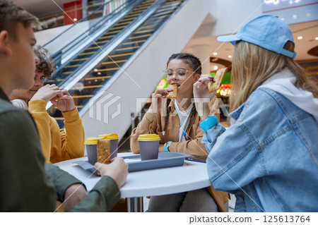 Teenage friends having snack drinking coffee at cafe in big city shopping center Teenage friends having snack drinking coffee at cafe in big city shopping center 125613764