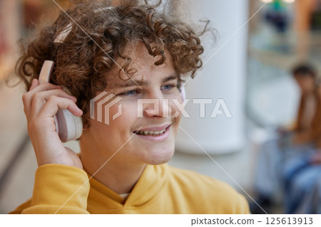 Teenage boy listening to music in headphones over shopping mall background Teenage boy listening to music in headphones over shopping mall background 125613913