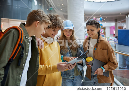 Happy young teenager showing photos on tablet mobile to friends in shopping mall 125613930