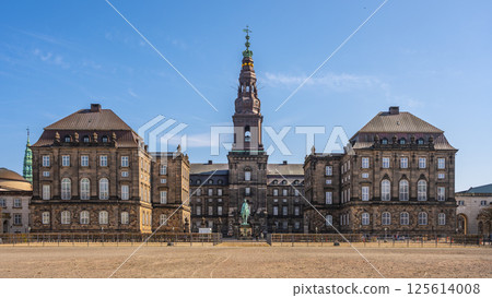 Christiansborg Palace stands majestically on Slotsholmen in Copenhagen. Visitors admire the historic architecture under a bright blue sky, showcasing Denmark's rich cultural heritage. Christiansborg Palace stands majestically on Slotsholmen in Copenhagen. Visitors admire the historic architecture under a bright blue sky, showcasing Denmark's rich cultural heritage. 125614008