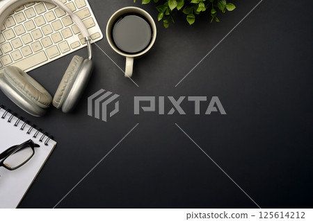Stylish black office desk with headphones, coffee cup, keyboard, notebook and glasses Stylish black office desk with headphones, coffee cup, keyboard, notebook and glasses 125614212