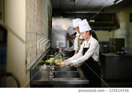 Culinary students washing fresh vegetables together at the sink 125614356