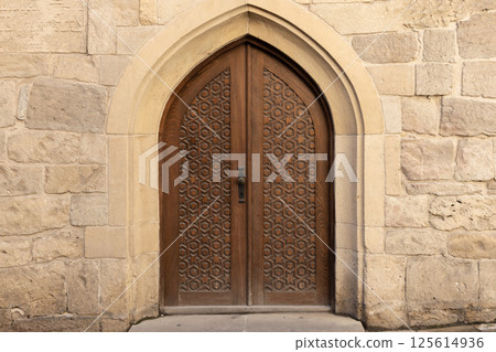 Beautiful handcrafted wooden door set within a detailed stone archway Beautiful handcrafted wooden door set within a detailed stone archway 125614936