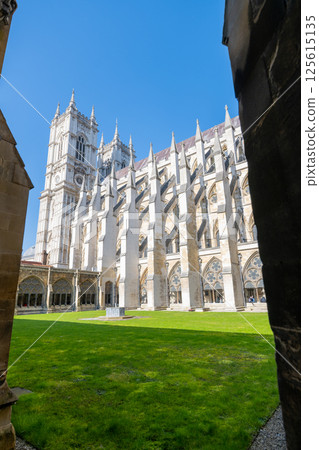 Visitors enjoy the serene green lawn surrounded by the stunning architecture of Westminster Abbey's cloisters on a bright, sunny day in London. The tranquil setting invites reflection and exploration. 125615135