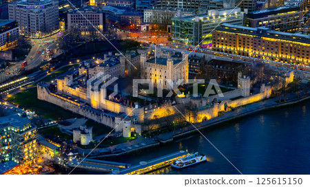A vibrant aerial view captures the illuminated Tower of London at dusk. The historic castle stands majestically beside the Thames, surrounded by the sparkling city lights of London. A vibrant aerial view captures the illuminated Tower of London at dusk. The historic castle stands majestically beside the Thames, surrounded by the sparkling city lights of London. 125615150