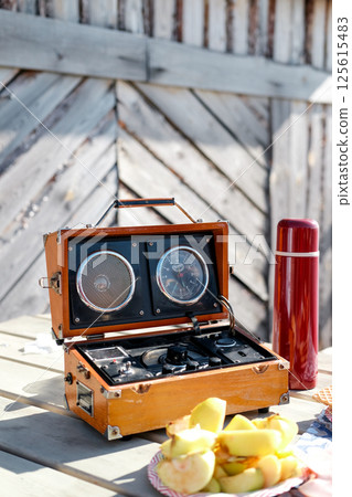 retro radio with mirror, red thermos and fruit snack on wooden table, sunny day retro radio with mirror, red thermos and fruit snack on wooden table, sunny day 125615483
