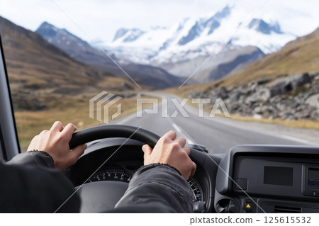 Driving towards majestic snowy mountain range POV, hands grip steering wheel on winding road, epic mountain landscape unfolds ahead, perfect for adventure travel mountain themed content. 125615532