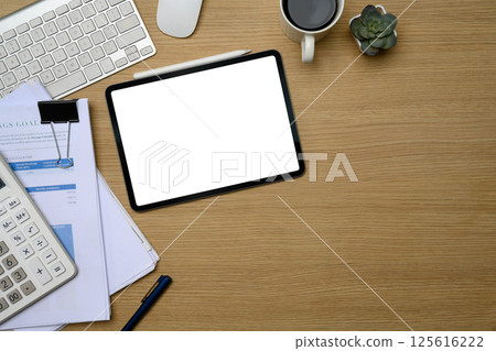 Digital tablet with blank screen on office desk surrounded by documents, calculator and coffee mug 125616222