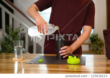 Young caucasian man preparing a protein shake in a cozy home kitchen Young caucasian man preparing a protein shake in a cozy home kitchen 125616223