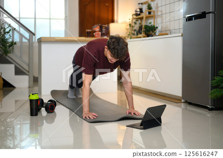 Active man doing plank exercise on mat and following an online workout on digital tablet 125616247