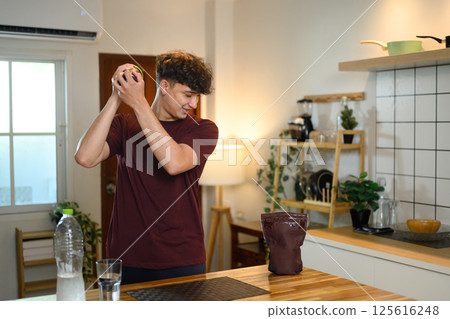 Man shaking a protein shaker bottle in a kitchen preparing nutritious fitness drink 125616248
