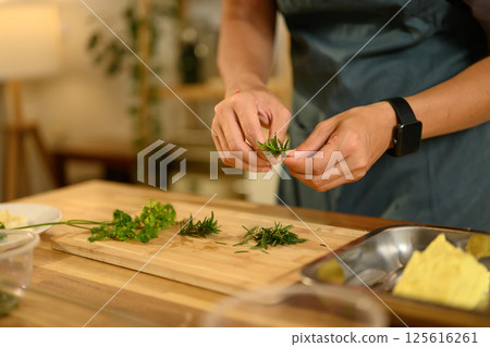 Man preparing fresh herbs on wooden cutting board for making compound butter in a kitchen 125616261