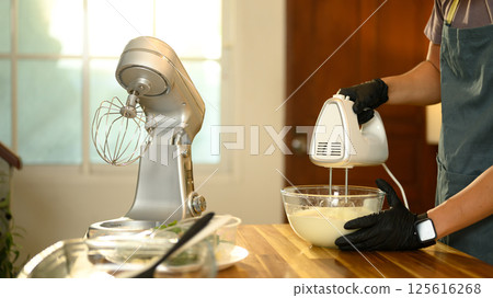 Young asian man using a hand mixer to churn cream in a glass bowl Young asian man using a hand mixer to churn cream in a glass bowl 125616268