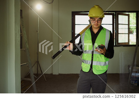 Construction worker holding sledgehammer and using smartphone at a construction site Construction worker holding sledgehammer and using smartphone at a construction site 125616302