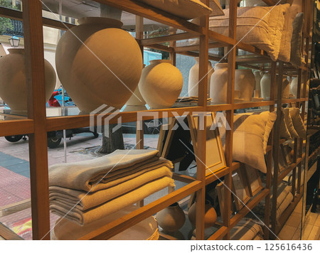 Earthenware vases and candle holders are arranged on a shelf, textured pillows in front, creating rustic scene. Artistically arranged earthenware vase 125616436