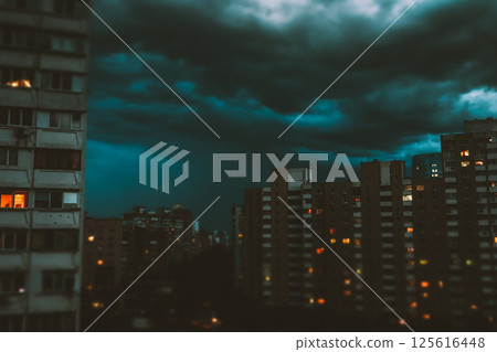 A night city with multi-story apartment buildings under dark blue stormy night cloudy sky. Lights are burning in the windows. Bedroom sleepy community A night city with multi-story apartment buildings under dark blue stormy night cloudy sky. Lights are burning in the windows. Bedroom sleepy community 125616448