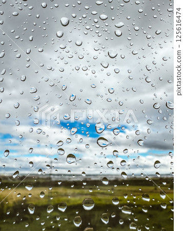 Extremely close up macro drops of water on a wet glass on natural green background. Raindrops pattern. Rainy day. Summer landscape through the window. 125616474