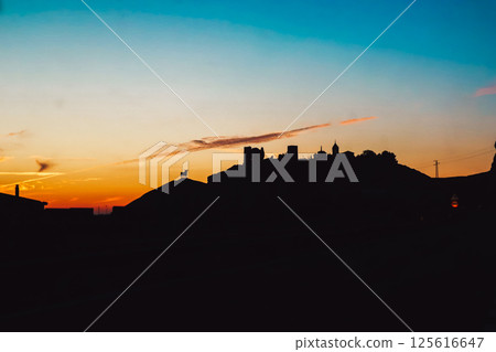 The castle on the mountain against the sunset sky. Abstract village, town in sunrise. Houses and towers on a hill at dusk, in twilight. Sunlight sky. 125616647