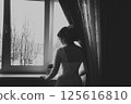 A girl in a wedding dress stands at the window with her back to the viewer. Black and white photo 125616810