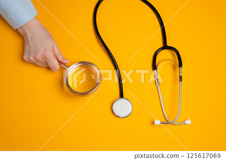 Concept of medical research, discovery and innovation. Analysis of medical services. Magnifying glass near stethoscope on a yellow background Concept of medical research, discovery and innovation. Analysis of medical services. Magnifying glass near stethoscope on a yellow background 125617069